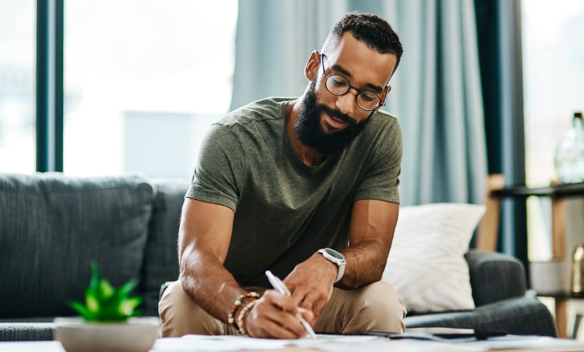 young man with beard writing in a journal.